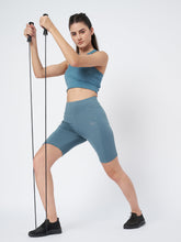Waylene's light blue high-waist cycling shorts worn by a woman using exercise resistance bands in a dynamic stretching pose, paired with a matching sports bra and black sneakers.