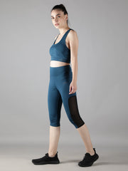 Side view of a model wearing Waylene's teal blue capri track suit set, walking to showcase the dynamic flexibility and stylish side mesh panels of the capris paired with a matching sports bra.