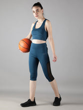 Waylene's teal blue sports bra and capri track suit set for women, featuring a model holding a basketball, showcasing mesh side panels on capris and a supportive sports bra. The model is posed in a side stance, highlighting the fit and functionality of the activewear.