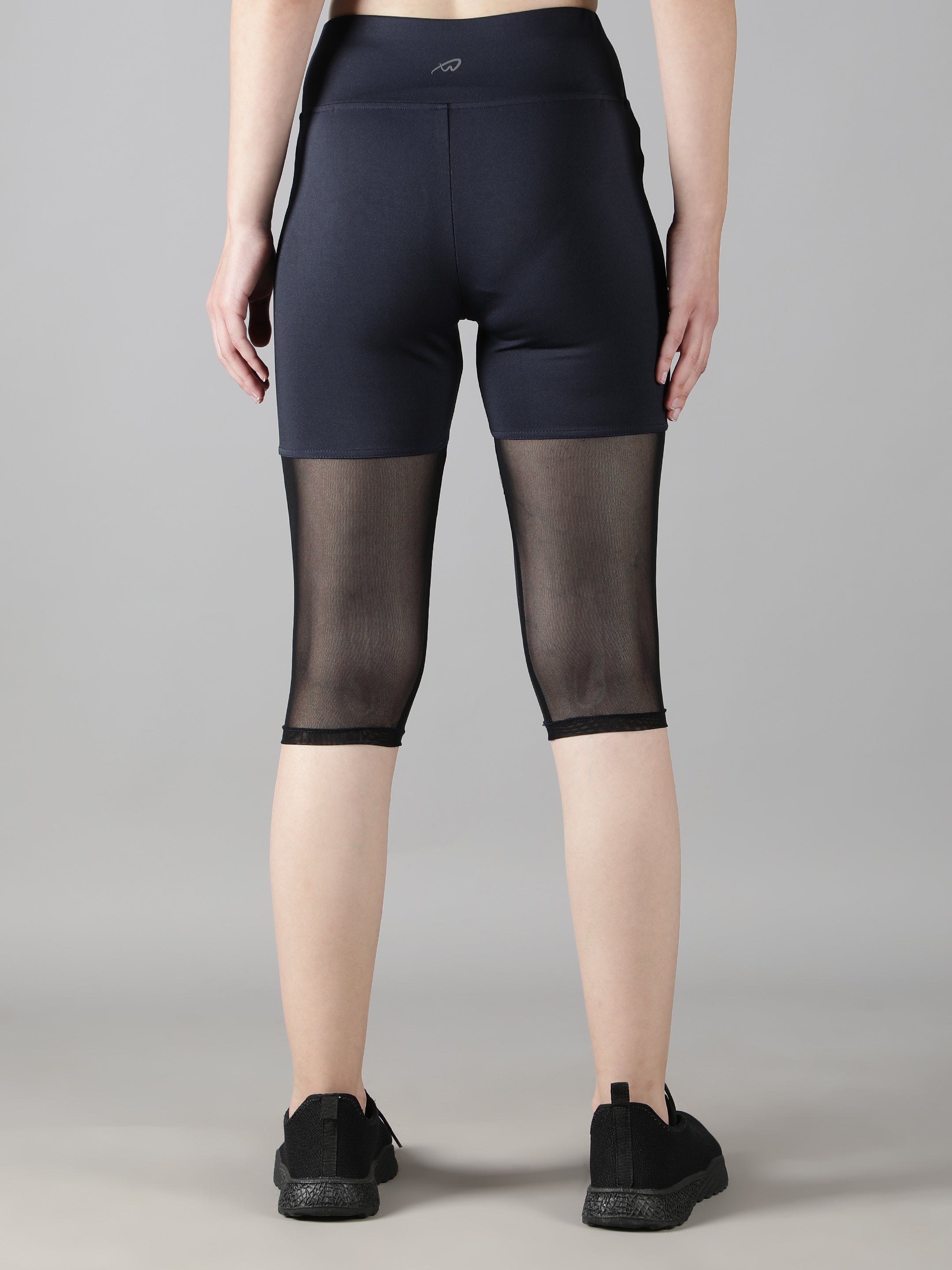 Back view of a model wearing Waylene's navy blue capri tights, showcasing the sheer mesh panels and high-rise design, tailored for sports and training.